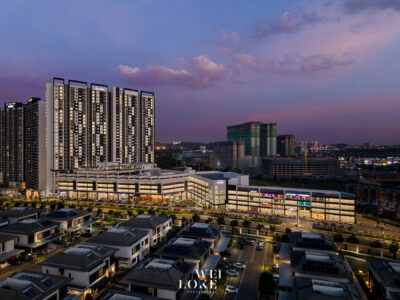 Aerial view of modern apartment towers and a shopping center at dusk, with a purple sky behind them.