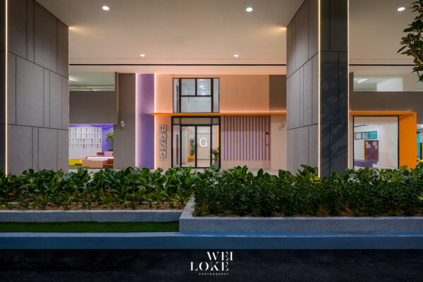 Nighttime view of a modern building entrance with purple column, orange awning, and glass doors displaying a large 'G' logo inside.
