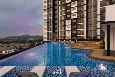 Outdoor rooftop pool beside a modern high-rise residential building at dusk, with lounge chairs and distant hills in a pastel sky